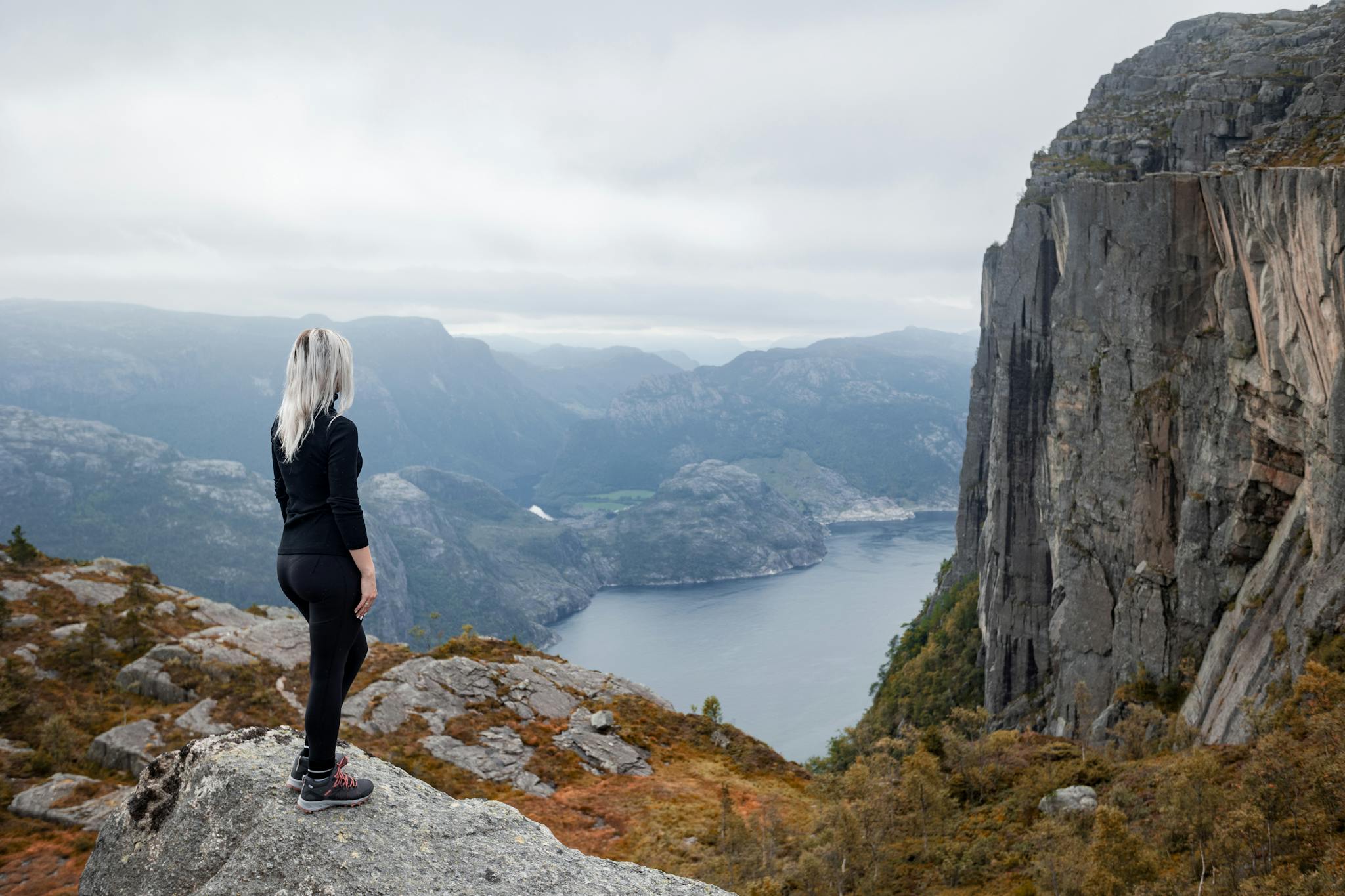 a girl standing on the edge of the cliff in the mountains on a hike in Norway on fjord